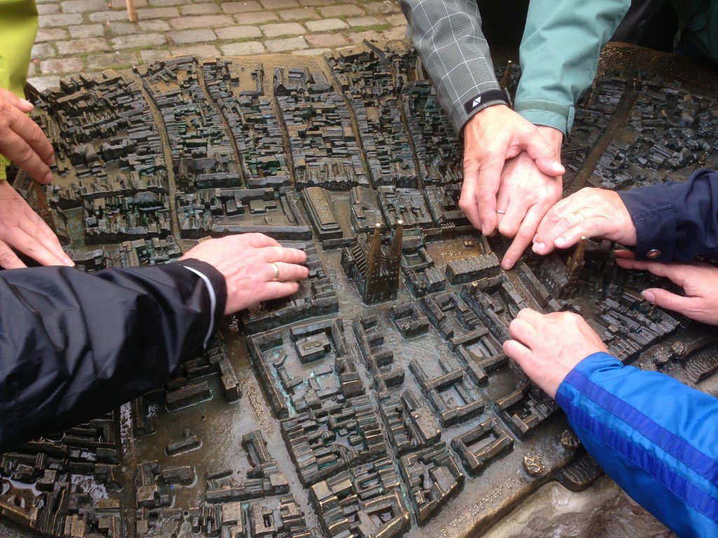 Sieben Hände ertasten das Bronzemodell der Lübecker Innenstadt. Eine der Hände wird von einer achten Hand geführt.