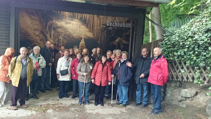 Gruppenfoto (mit 23 Personen) vor dem Eingang der Dechenhöhle. An der Wand ist ein großes Foto aus der Dechenhöhle angebracht.